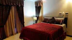 Une chambre d’hôtel avec un lit, des rideaux, une lampe de chevet et un téléphone fixé au mur.