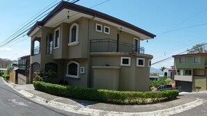 Une maison à deux étages avec un balcon, une allée et une haie bien entretenue.