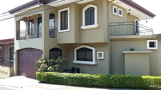 Une maison à deux étages avec un balcon, un garage et une haie bien entretenue.