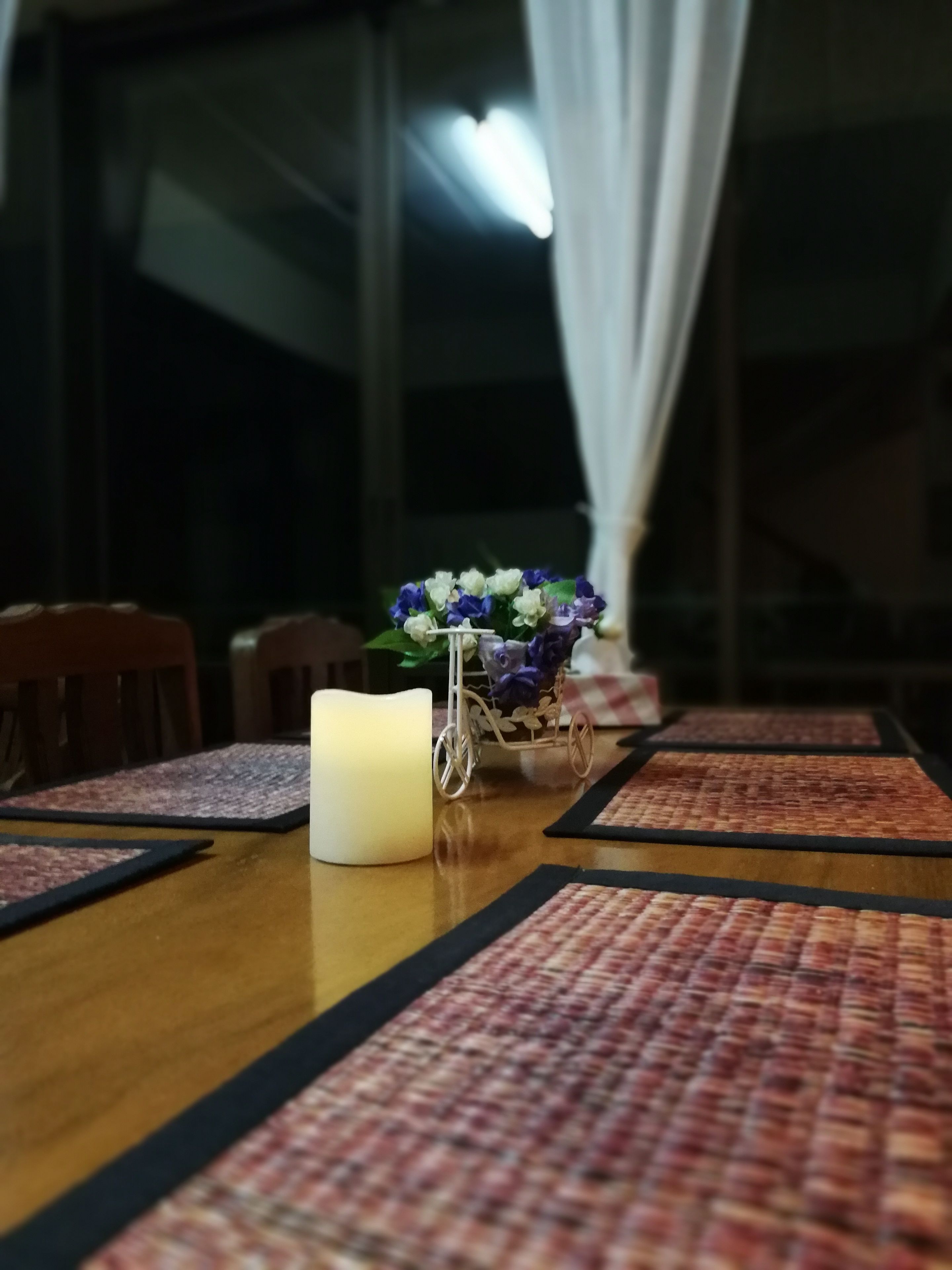 A dining table with a candle, placemats, and a vase of flowers.