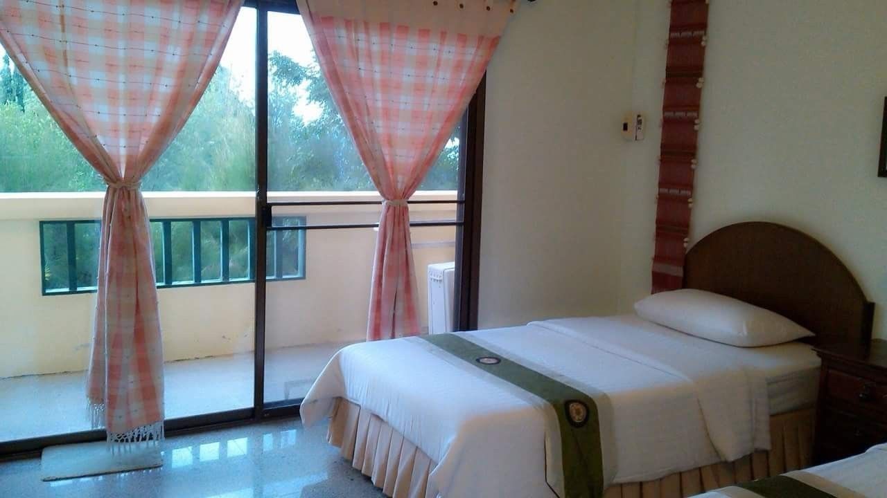 A bedroom with a bed, a window with curtains, and a view of greenery outside.