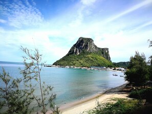 Uma área costeira com uma colina rochosa imponente, uma praia de areia e um cais com barcos.