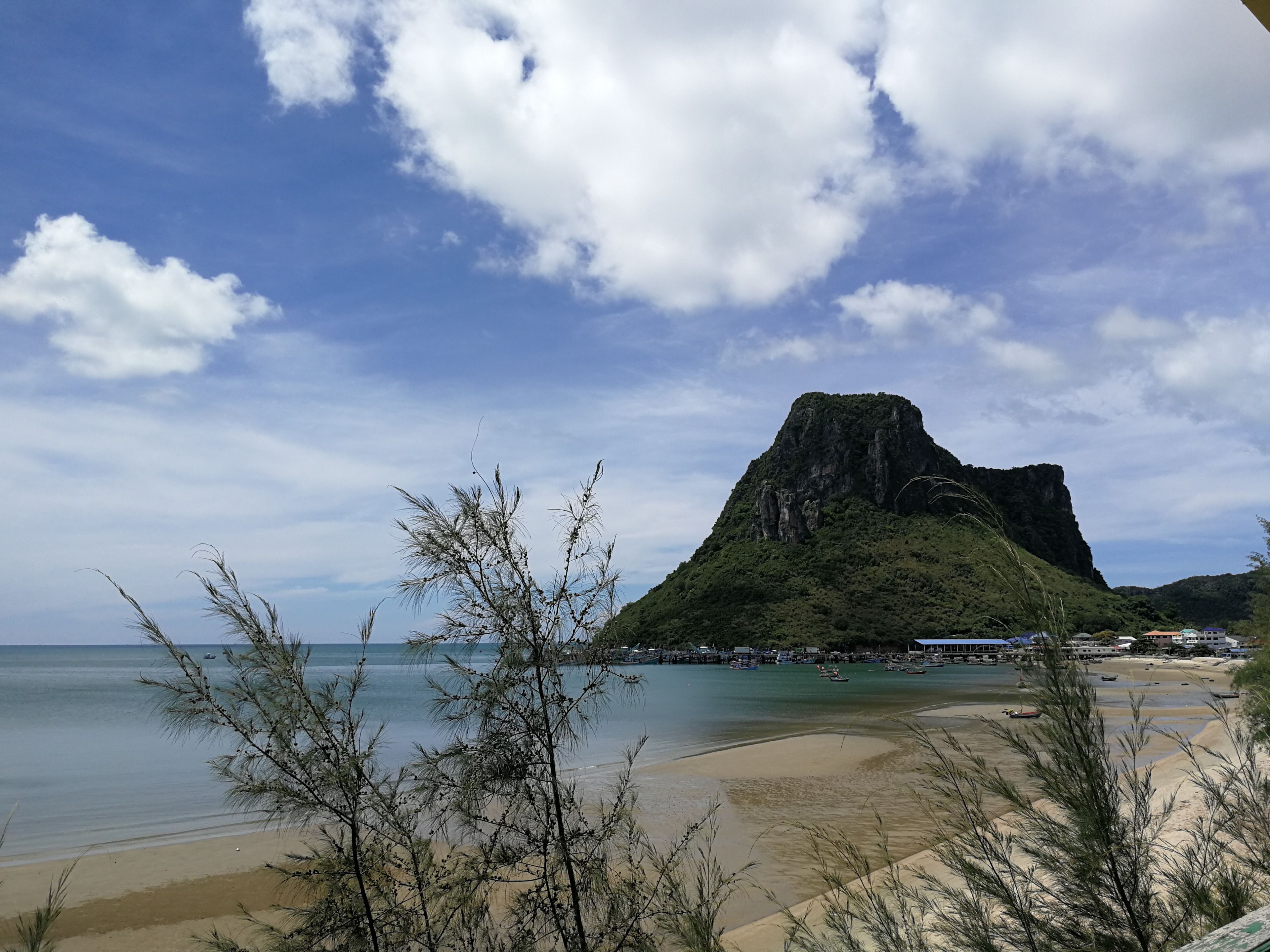 A beach with a prominent mountain in the background, clear skies, and calm waters.