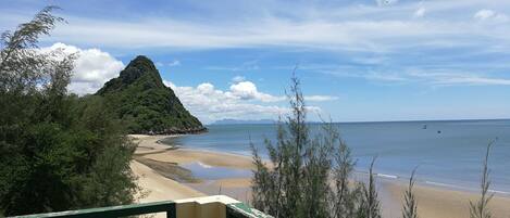 Una playa con una montaña, cielo despejado y mar tranquilo.