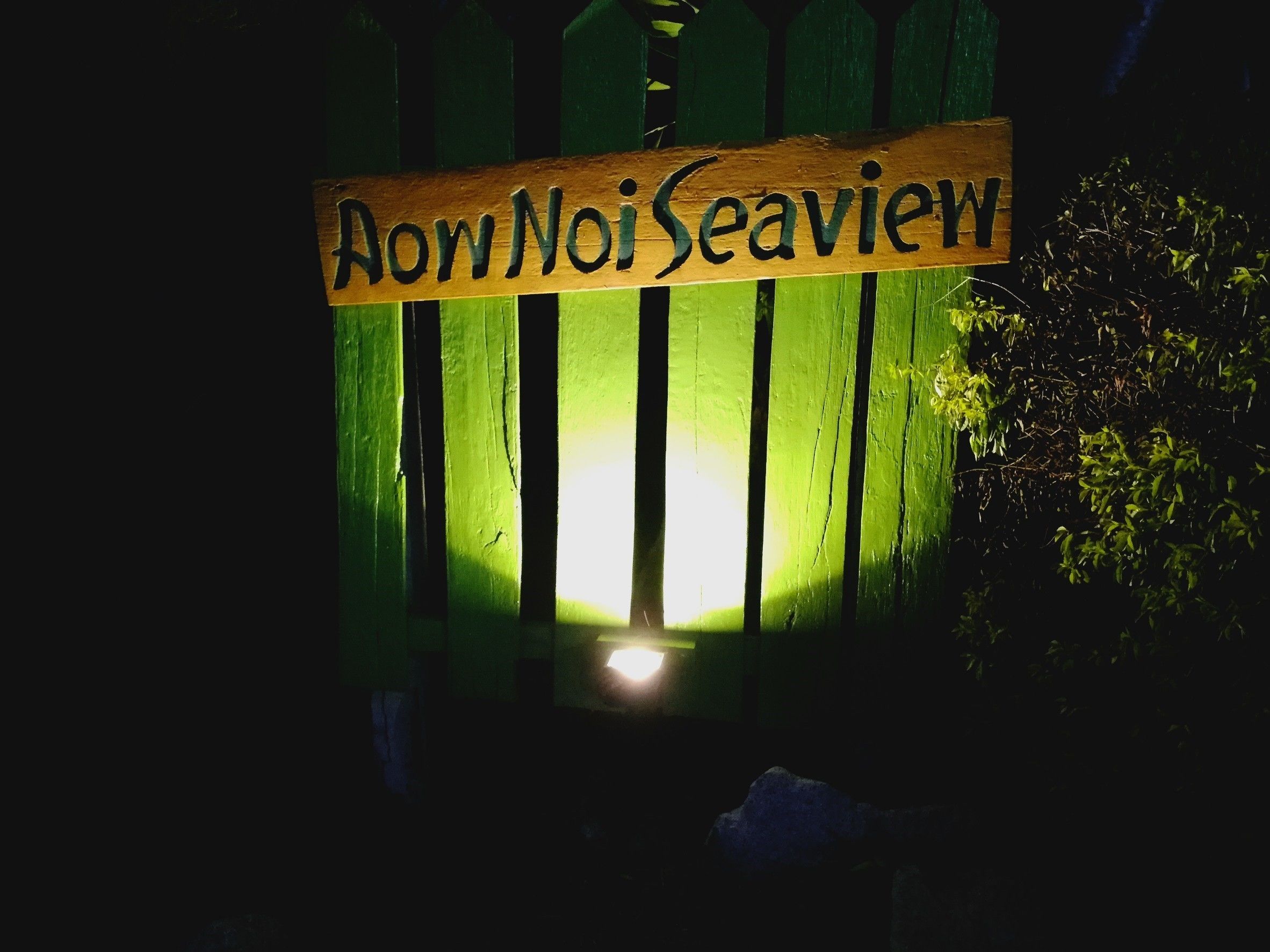 Een houten bord met de tekst 'Aon Noi Seaview' verlicht met een lamp.