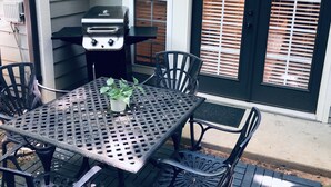 Un patio al aire libre con una mesa y sillas de metal, una parrilla y una puerta con persianas.
