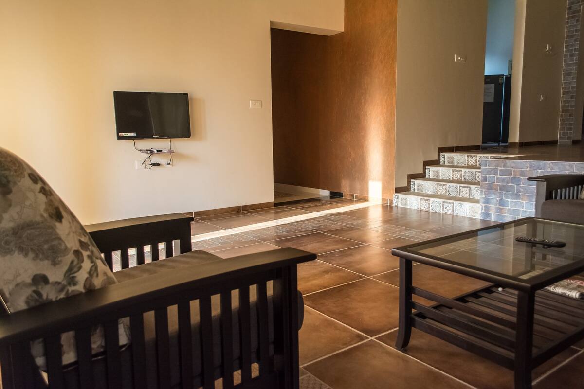 Una sala de estar moderna con un televisor de pantalla plana montado en la pared, una mesa de centro de vidrio y un banco de madera oscura.