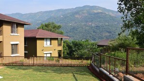 A yellow building with a red roof, surrounded by a fenced yard and greenery. - 3BHK by Tripvillas Holiday Homes (Paud)