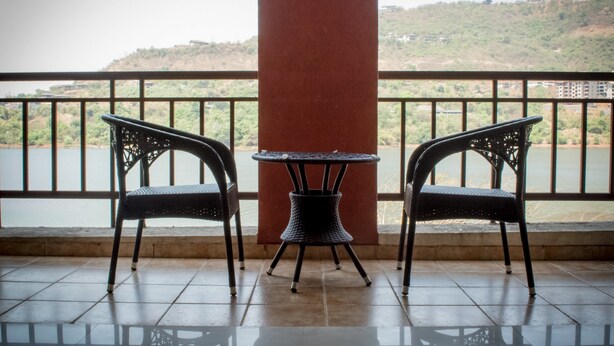 A balcony with two chairs and a table, overlooking a body of water and a hilly landscape. - 3BHK by Tripvillas Holiday Homes (Paud)