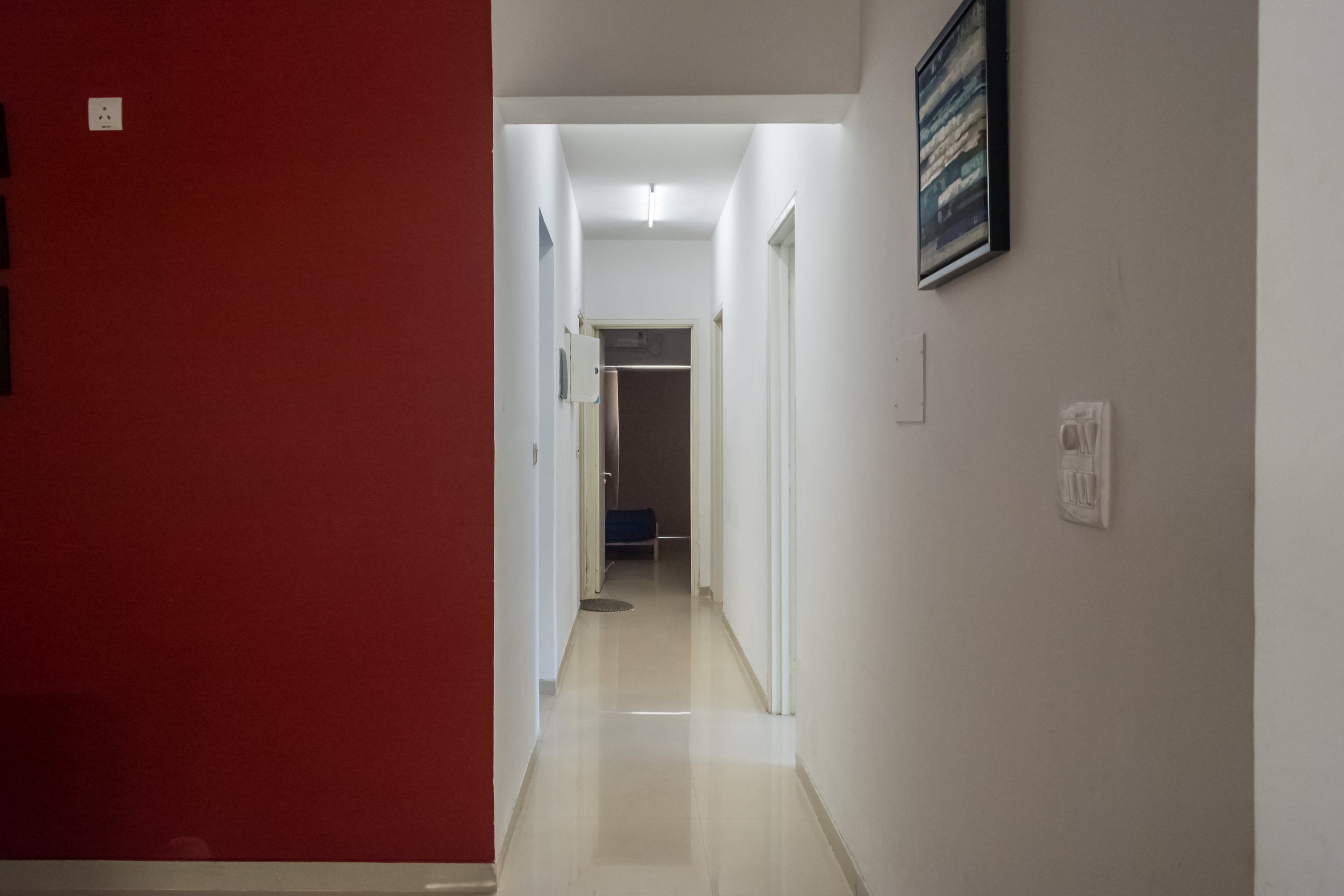 Un couloir avec un mur rouge à gauche et un mur blanc à droite, qui mène à une pièce dont la porte se trouve au fond.