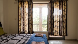 A room with a bed, a window with curtains, and a view of trees outside.