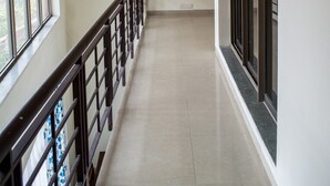 A corridor with a tiled floor, a wooden railing, and large windows on one side.
