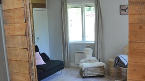 A cozy room with a wooden floor, a dark sofa, a fluffy chair, and a window with curtains. - Grab your chance! Our plans have changed making Nickebo bookable after all! (Torsby)