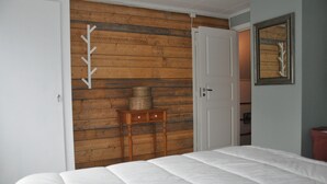 A bedroom with a wooden wall, a bed, a small wooden nightstand, and a door. - Grab your chance! Our plans have changed making Nickebo bookable after all! (Torsby)