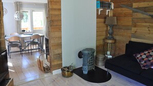 A cozy living room with a black sofa, a wooden wall, a small table with chairs, and a stove. - Grab your chance! Our plans have changed making Nickebo bookable after all! (Torsby)