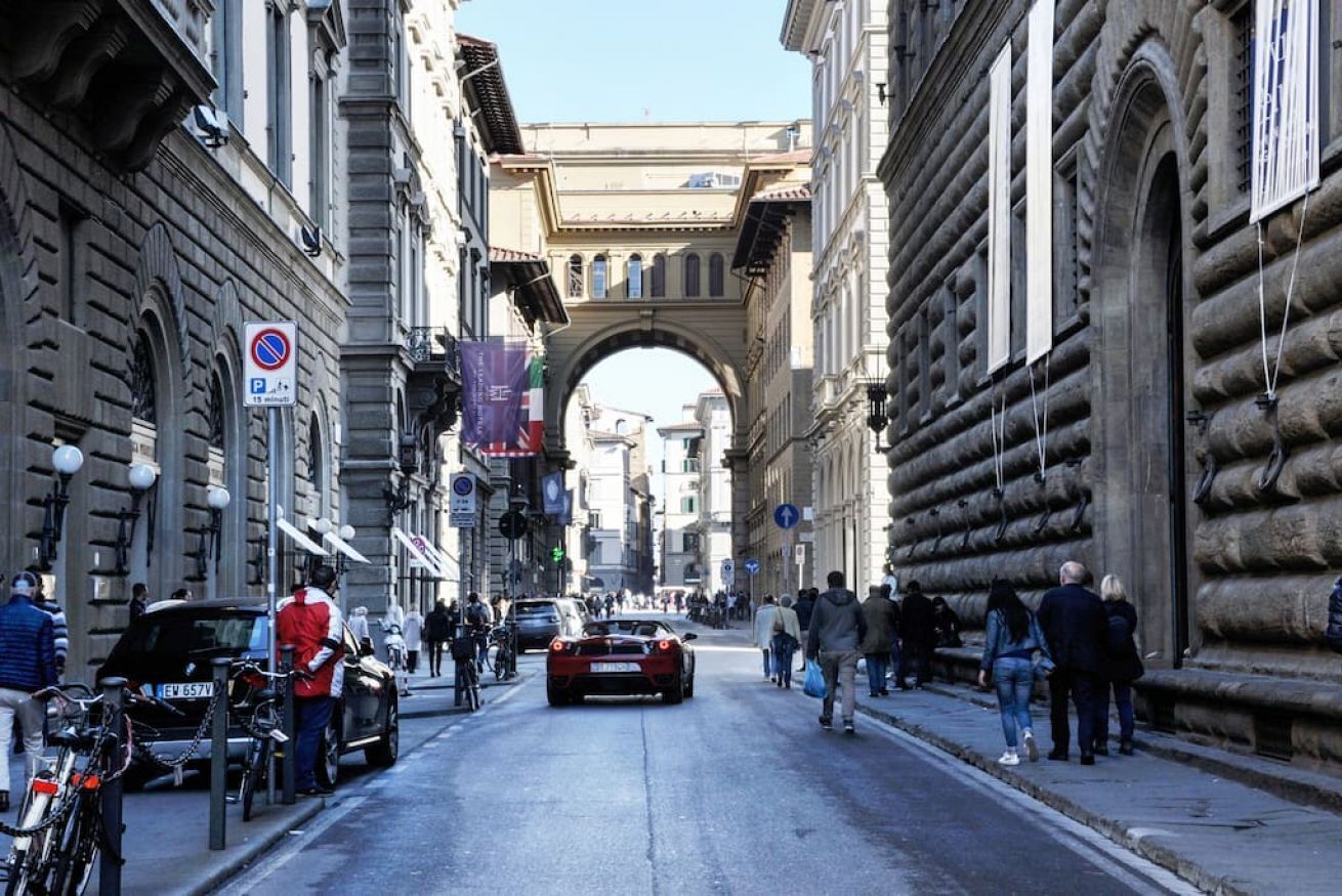 A street with historic buildings, a no parking sign, and a red sports car.