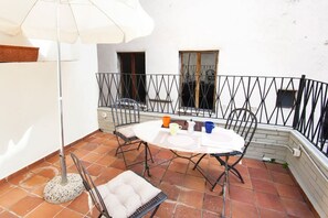 Une terrasse avec une table ronde, des chaises, un parasol blanc et une rambarde en métal.