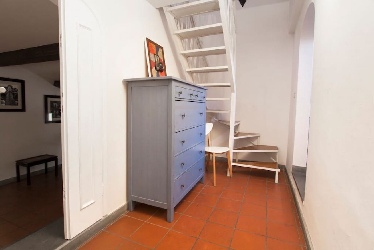 A narrow hallway with a blue dresser, a white chair, and a spiral staircase.