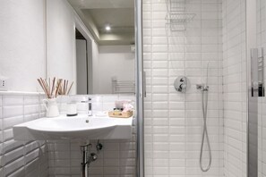 Une salle de bain avec un lavabo blanc, une cabine de douche en verre et un mur recouvert de carreaux blancs.