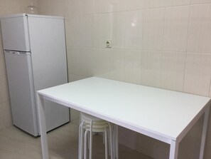 A small kitchen with a white refrigerator, a white table, and a white stool. - APARTMENT LISBON - REBOLEIRA (metro / train) (Amadora)