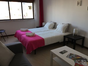 A hotel room with two beds, a small table, a chair, and a window with curtains. - APARTMENT LISBON - REBOLEIRA (metro / train) (Amadora)