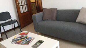 A living room with a grey sofa, a black chair, and a white coffee table with magazines and a remote control. - APARTMENT LISBON - REBOLEIRA (metro / train) (Amadora)