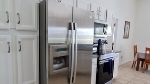 Une cuisine équipée d’un réfrigérateur en acier inoxydable, de meubles blancs, d’un four à micro-ondes et d’un coin repas avec des chaises et une table.