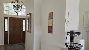 Un couloir orné d’un lustre, avec une porte en bois, un tableau encadré et une enseigne fixée au mur.