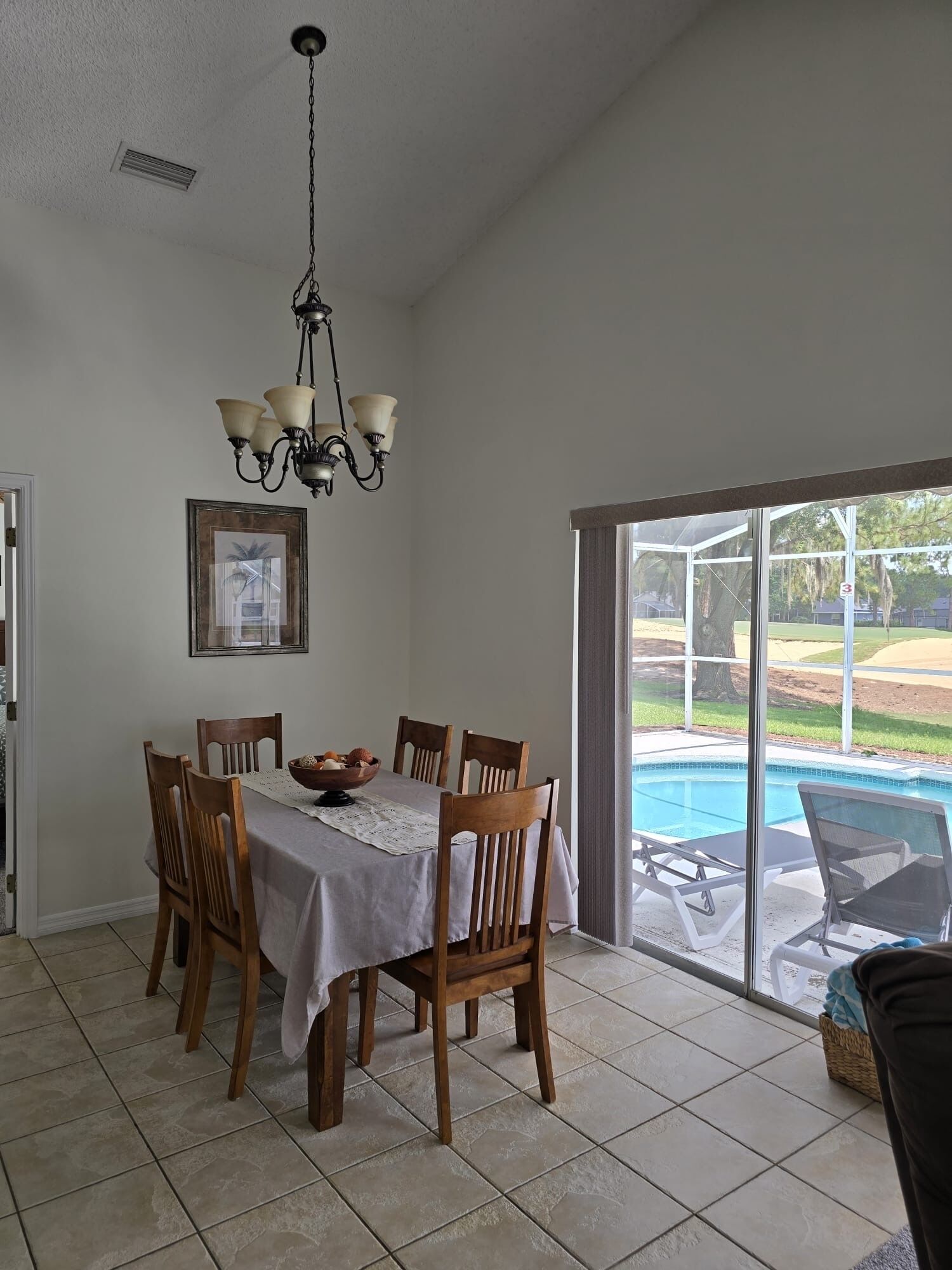 A dining area with a table set for six, a chandelier, and a view of a swimming pool through large glass doors.