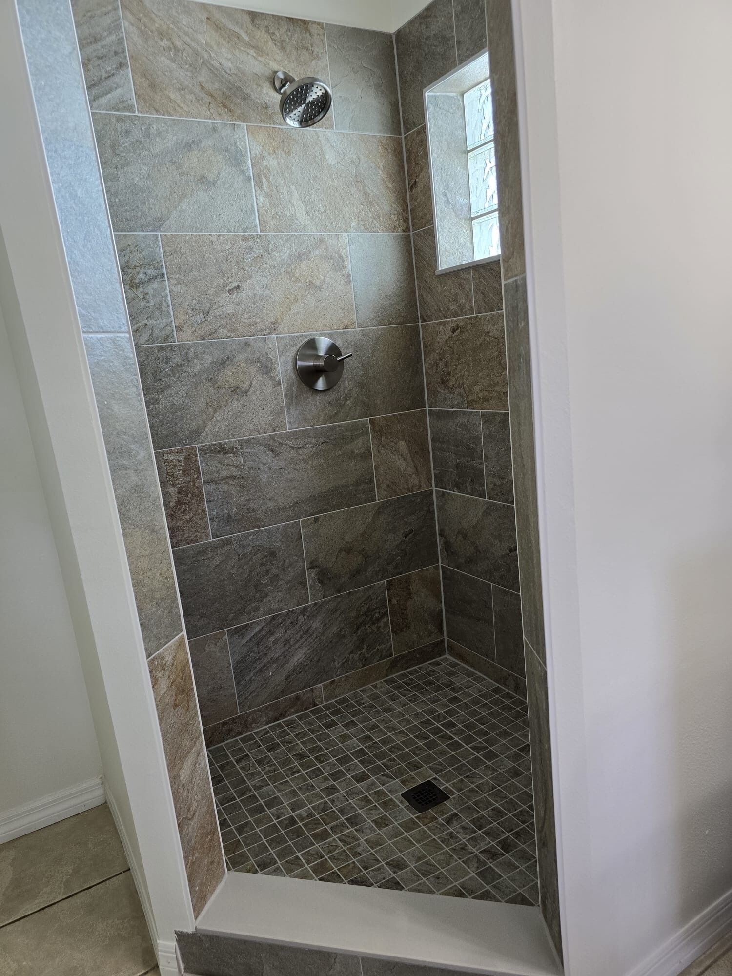 A shower area with stone tiles and a metal showerhead.
