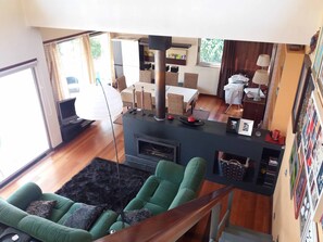 Een moderne woonkamer met een open haard, een groene bank en een eethoek met rieten meubels.