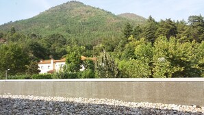Une vue d’un bâtiment avec un toit recouvert de tuiles, entouré d’arbres et avec une colline en arrière-plan.