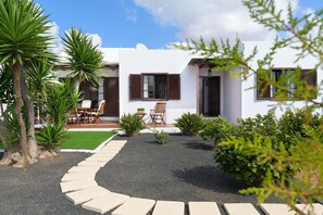 Un bâtiment blanc doté d’un patio, d’un espace extérieur aménagé avec des sièges et d’un chemin de gravier.