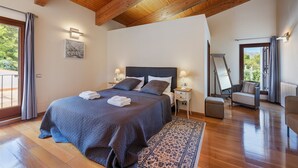 Una camera da letto con un letto grande, travi in legno a soffitto, un comodino con una lampada, una sedia e vista sull'esterno da una finestra.