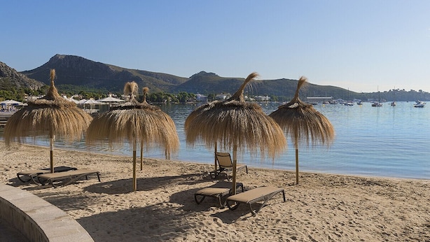 Una spiaggia con ombrelloni di paglia, sdraio e un mare calmo con barche sullo sfondo.