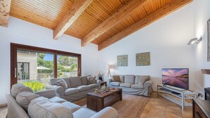 Un soggiorno spazioso con soffitto in legno, ampie finestre, una televisione a schermo piatto e un'area salotto confortevole.