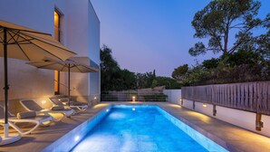 Una piscina con lettini e ombrelloni, circondata da una recinzione in legno e alberi.
