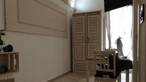 Una habitación con un armario de madera, una silla blanca y una mesita.
