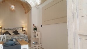 Un dormitorio con cama, mesitas de noche, lámpara, una pequeña mesa con un cuenco y utensilios, y una lámpara colgante decorativa.