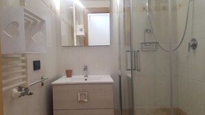 Un baño con cabina de ducha de vidrio, un lavabo con espejo y un armario de madera.