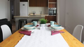 A modern kitchen with wooden cabinets, a built-in oven, and a dining area with a wooden table set for two. - Atico73 Tourist Housing  (Medina-Sidonia)