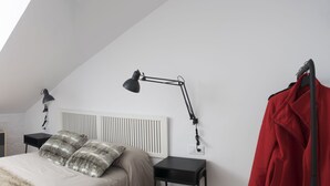A bedroom with a sloped ceiling, a bed with fluffy pillows, a white chair, a red coat hanging, and two bedside tables with lamps. - Atico73 Tourist Housing  (Medina-Sidonia)