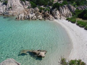 Une plage à l’eau turquoise et limpide, au sable blanc et aux formations rocheuses.