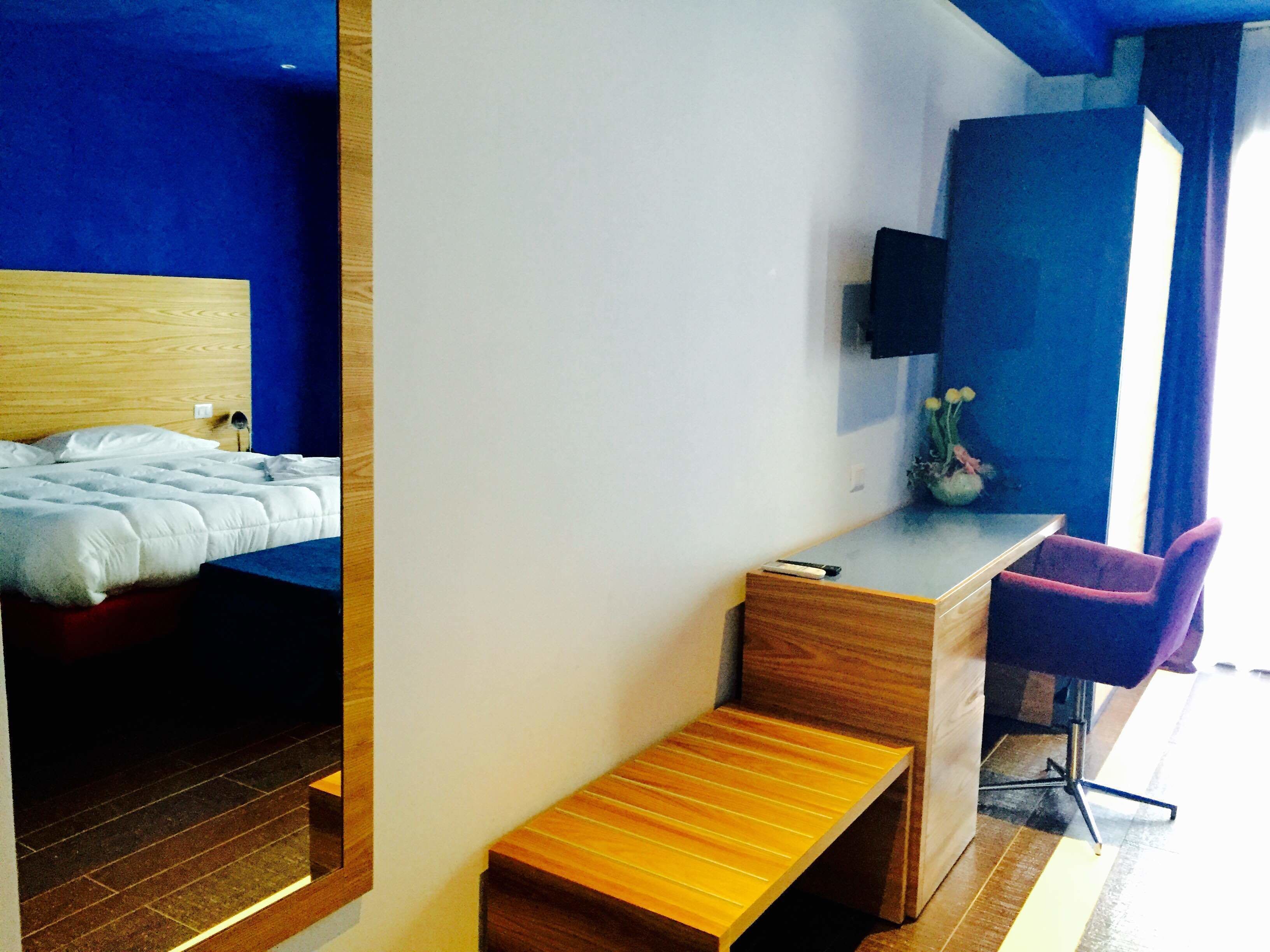 Una habitación de hotel moderna con una cama de madera, un escritorio con una silla y un pequeño banco.