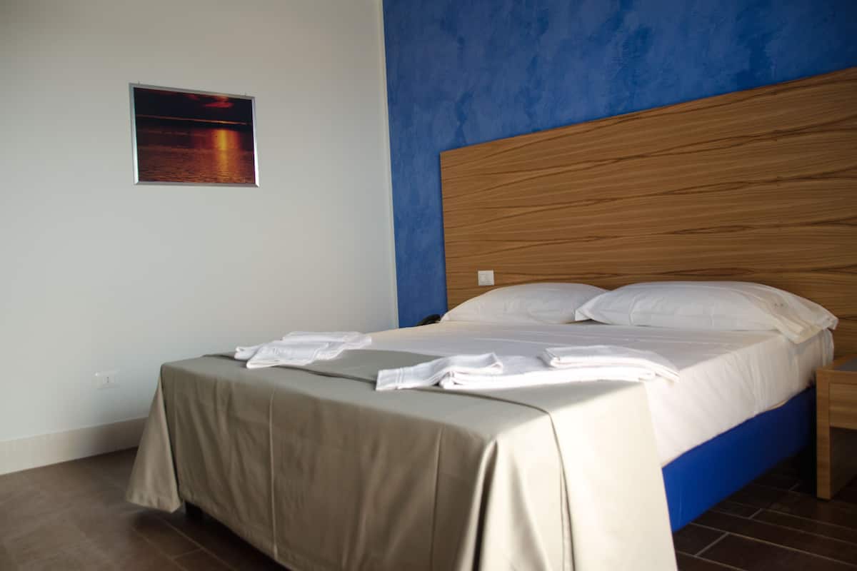A neatly made bed with a wooden headboard, a bedside table, and a framed picture on the wall.