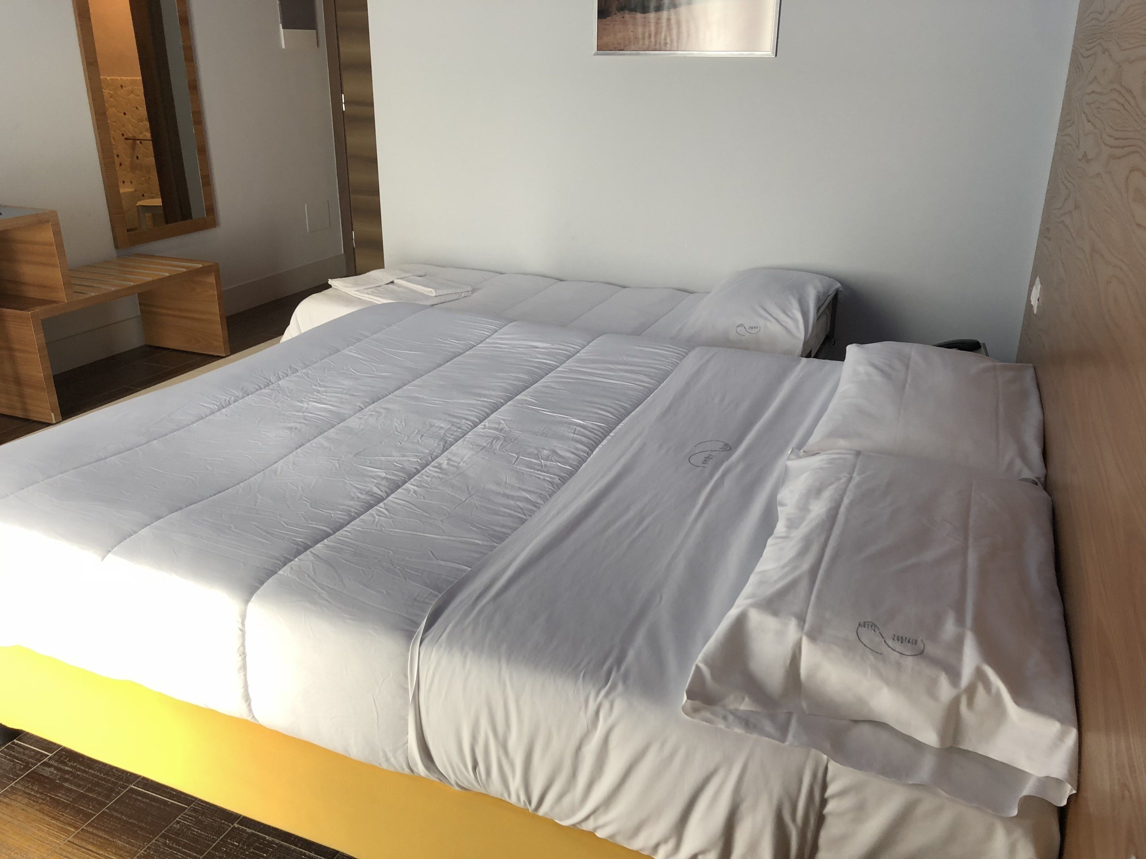 A neatly made double bed with white linens, a wooden headboard, and a small bedside table.