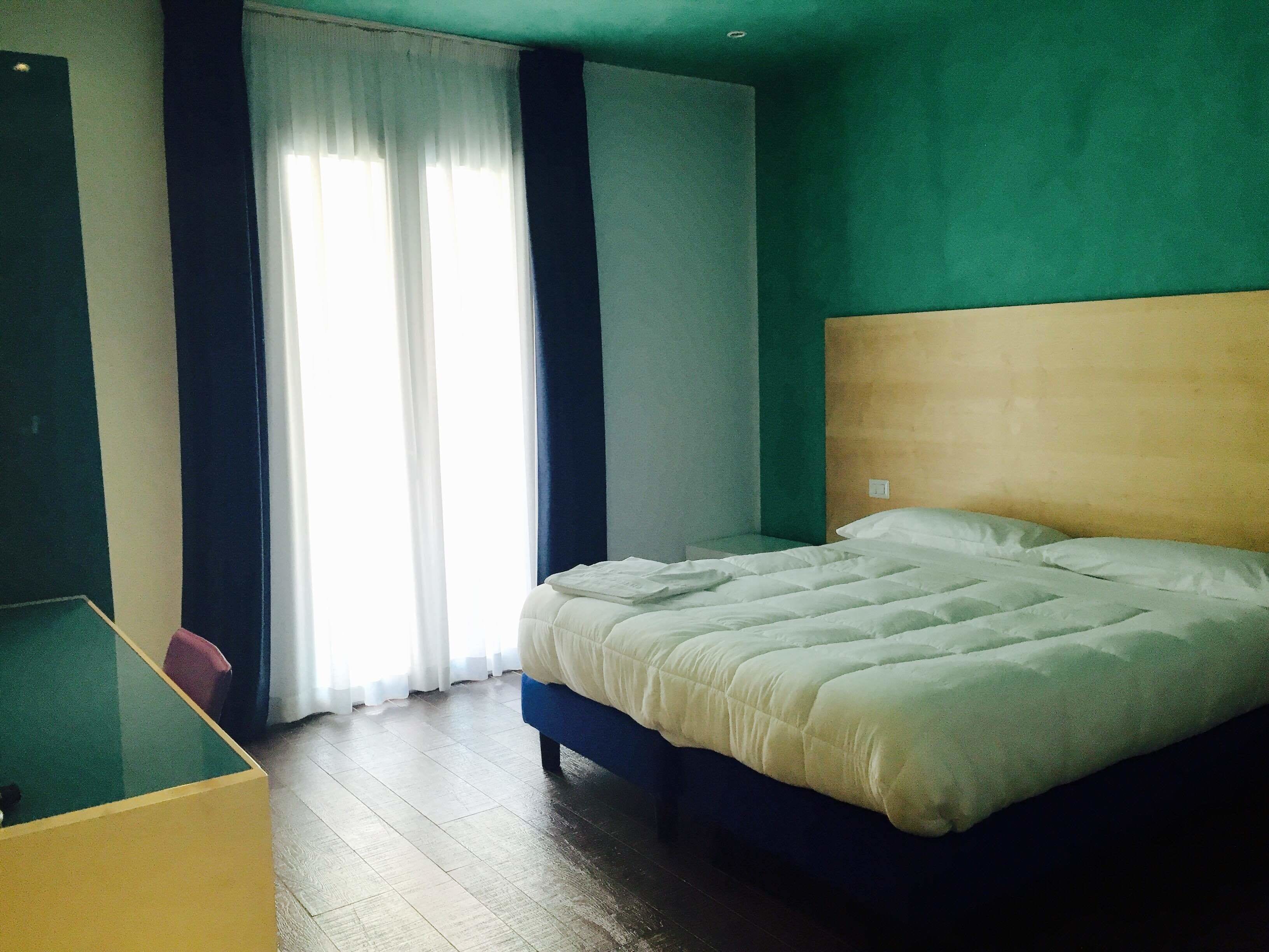 Une chambre d’hôtel avec un lit, un bureau et une fenêtre avec des rideaux.
