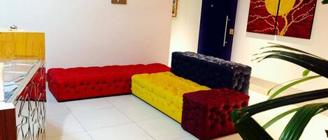 A modern living room with a sectional sofa in red, yellow, and blue, a flat-screen TV, and a door with a red and yellow abstract painting.