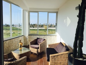 Ein Balkon mit Korbmöbeln, einem Glastisch und Blick auf eine grüne Landschaft.