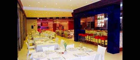 A dining area with tables set for service, a bar area with stools, and a stage in the background.